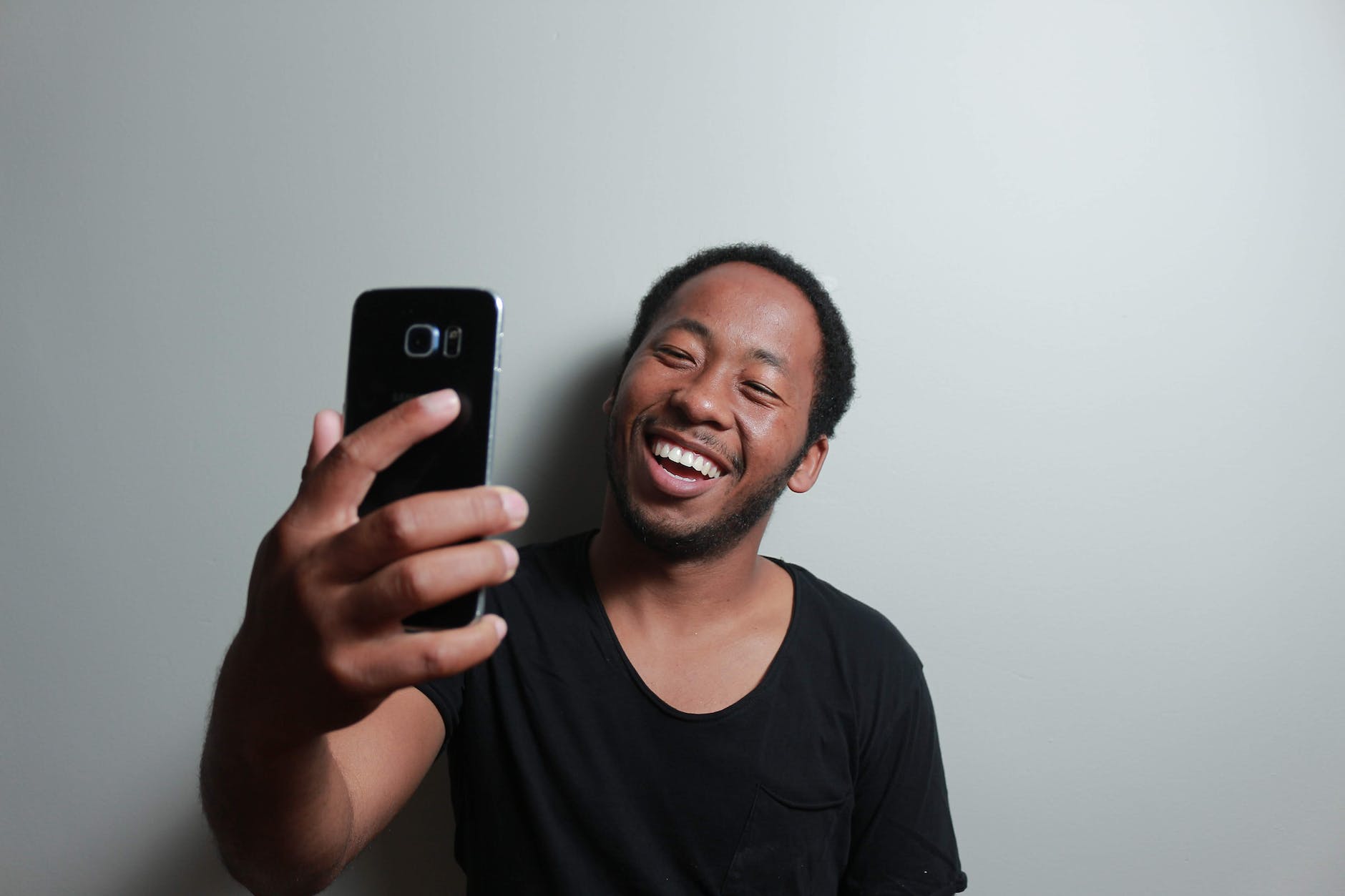 man holding smartphone while leaning on white wall